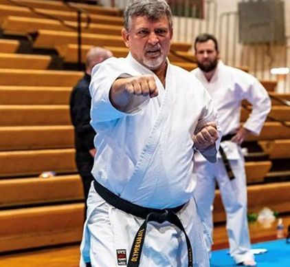 A man in a white karate uniform is pointing at the camera.