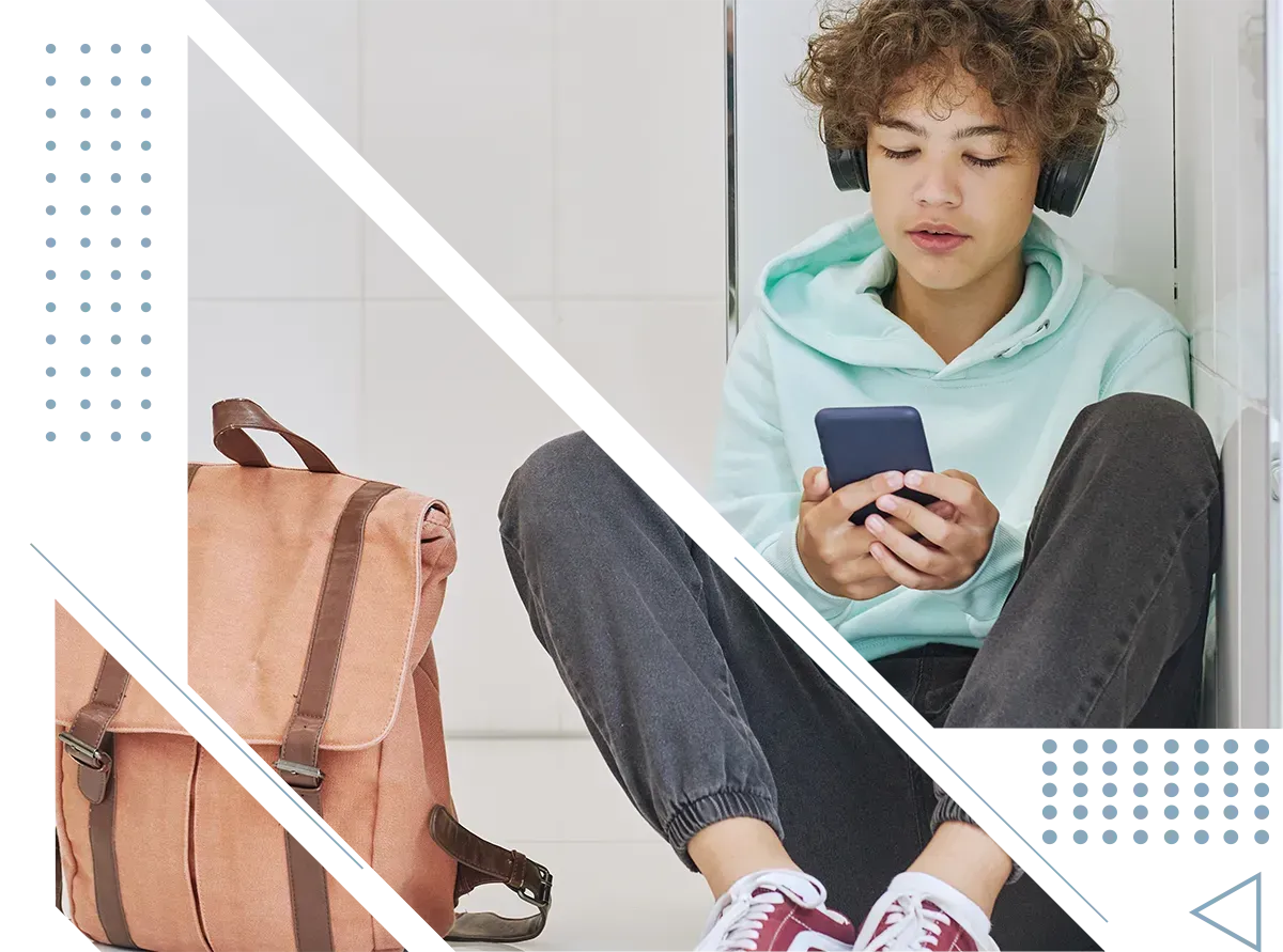 A young boy is sitting on the floor looking at his cell phone.