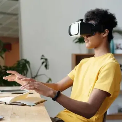 A young man wearing a virtual reality headset is sitting at a table.