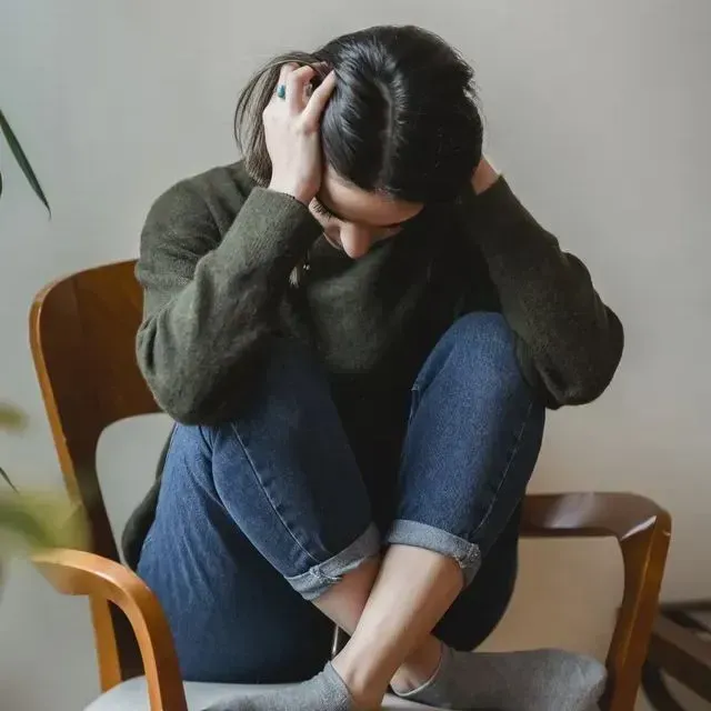 A woman is sitting in a chair with her head in her hands