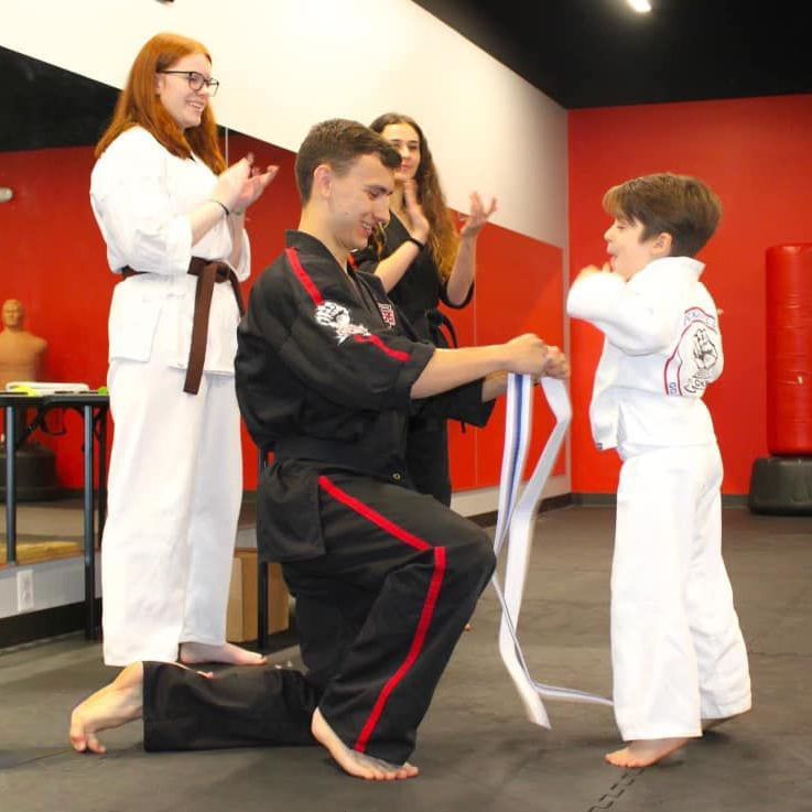 A man in a black karate uniform is kneeling down next to a boy in a white karate uniform