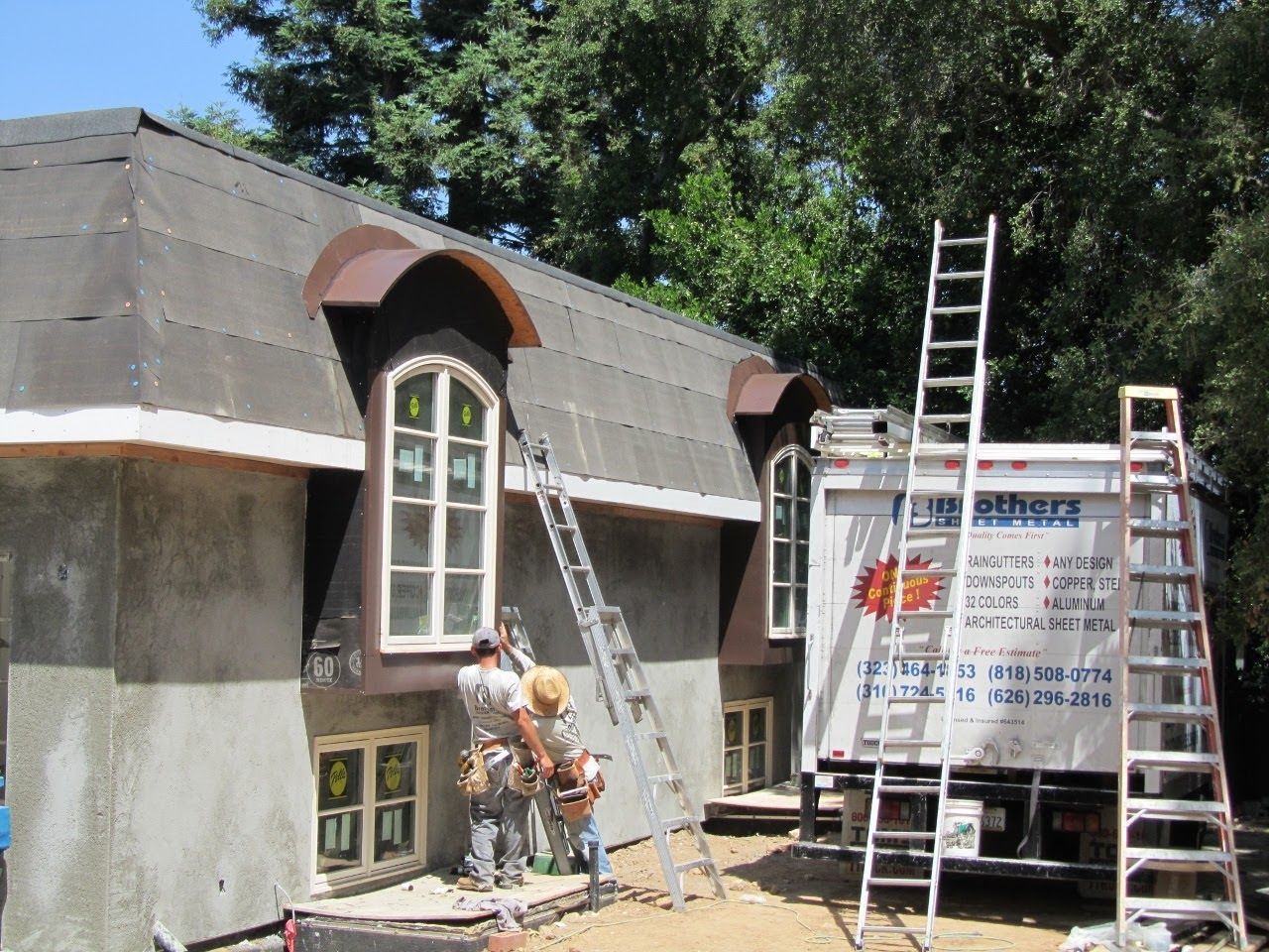 Construction workers on scaffolding near a truck installing roofing shingles on a two-story house.