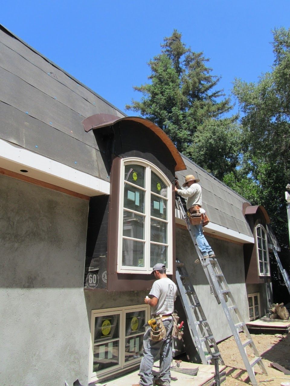 Construction workers installing windows on a two-story house with a curved roof section, blue sky.