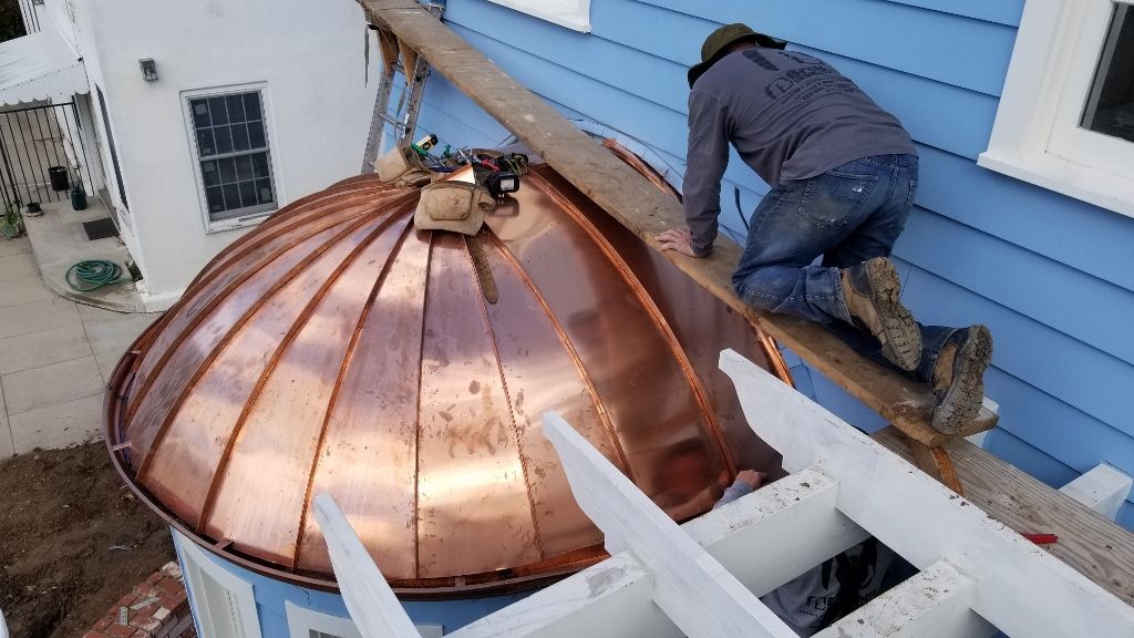 A worker installs a copper dome roof on a blue building.
