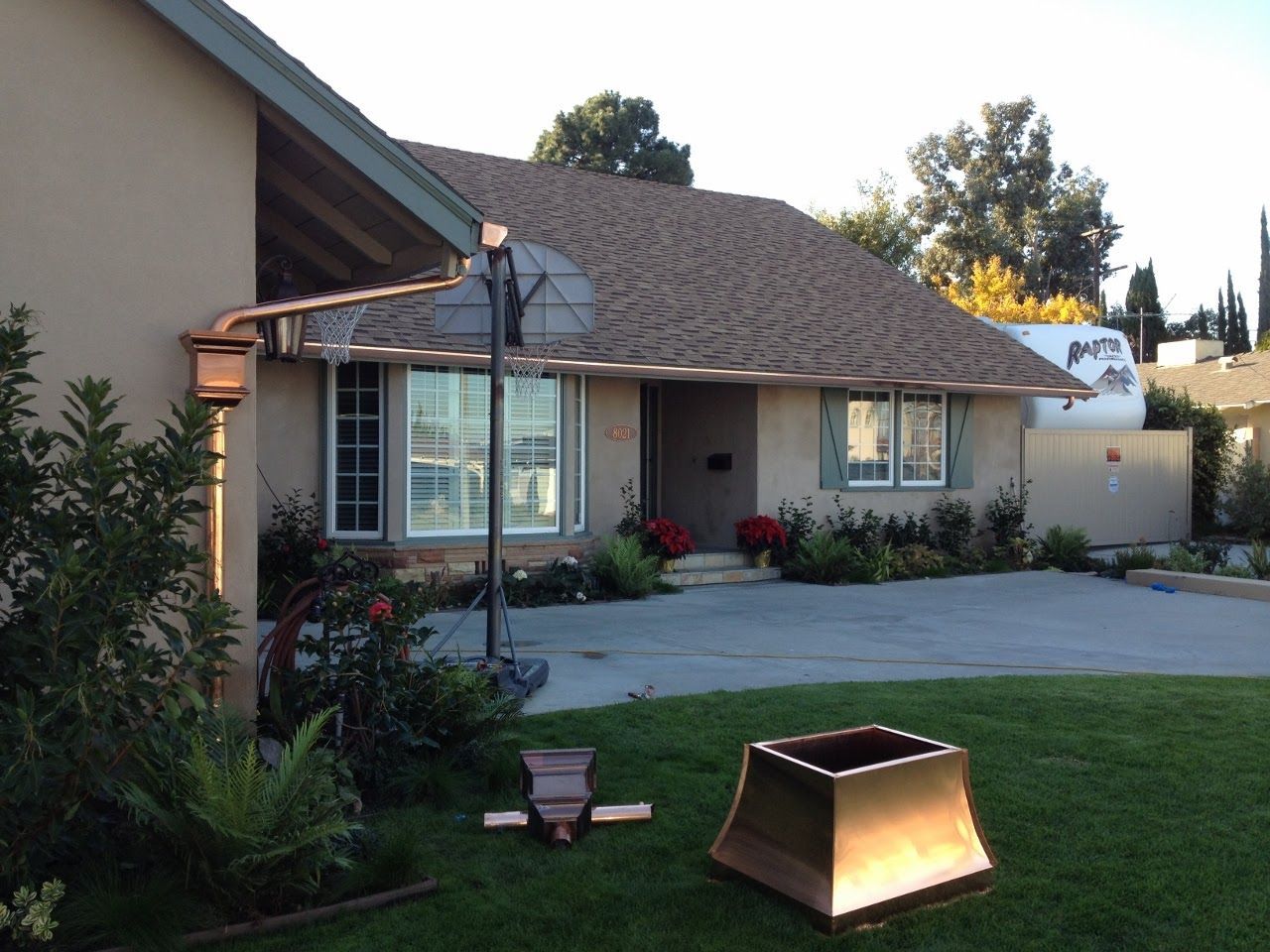Copper gutters and downspouts on a house with a brown roof. Lawn and driveway in the foreground.