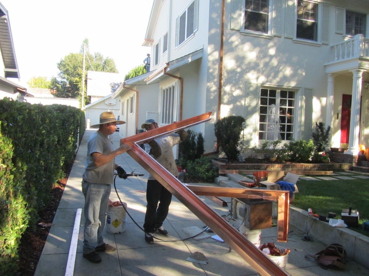 Two men working with copper gutter material outside a white house.