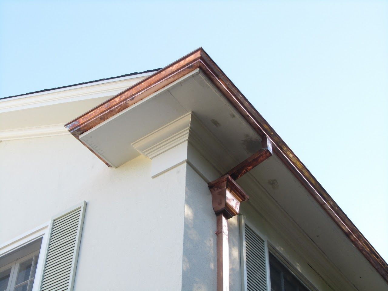 Copper gutters on a white house corner with a light blue sky above.
