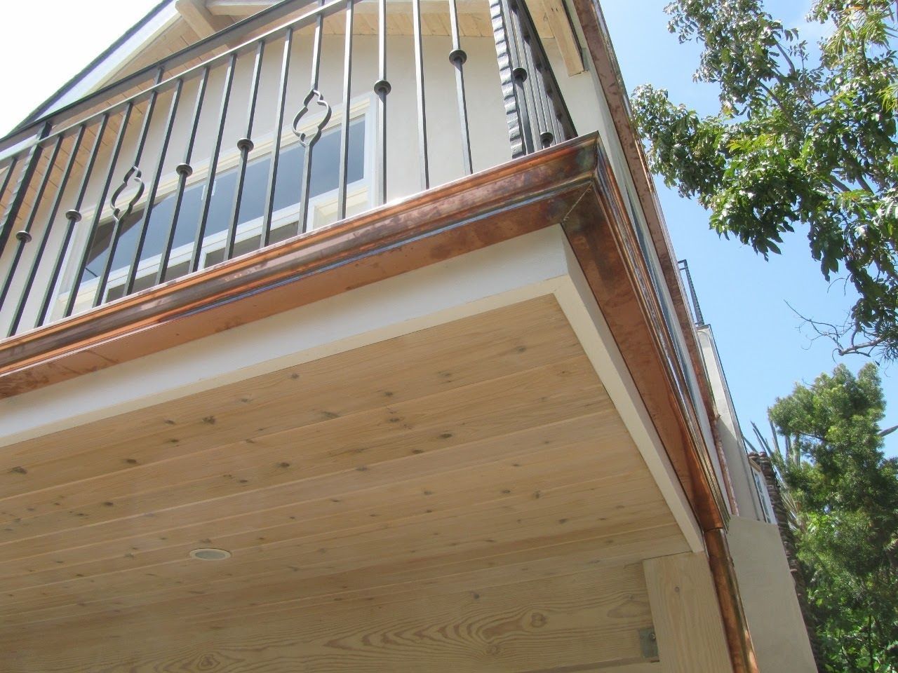 Wooden deck with copper trim and black railing, viewed from below against a blue sky.