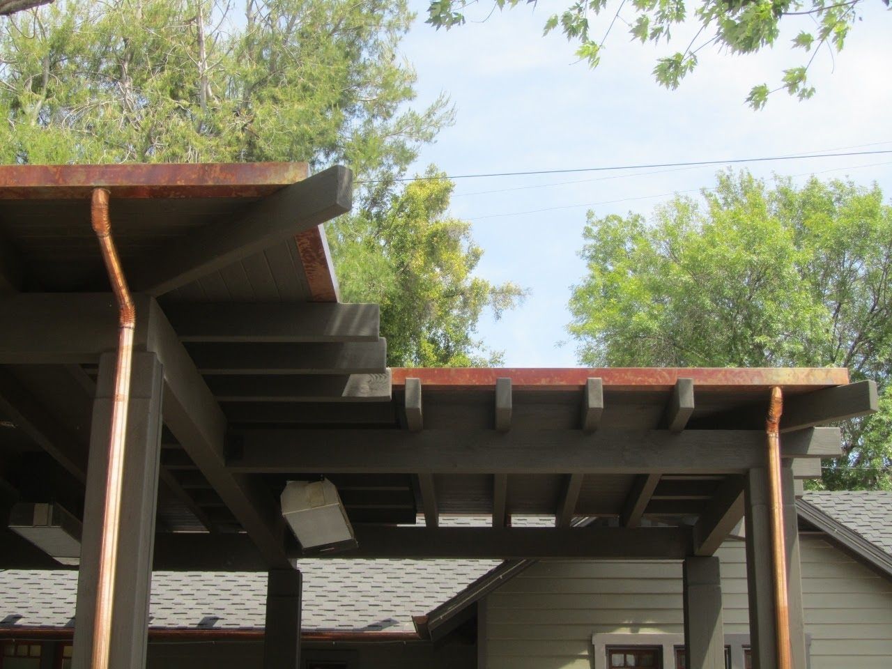 Copper gutters on a brown pergola, house in the background, sunny day.