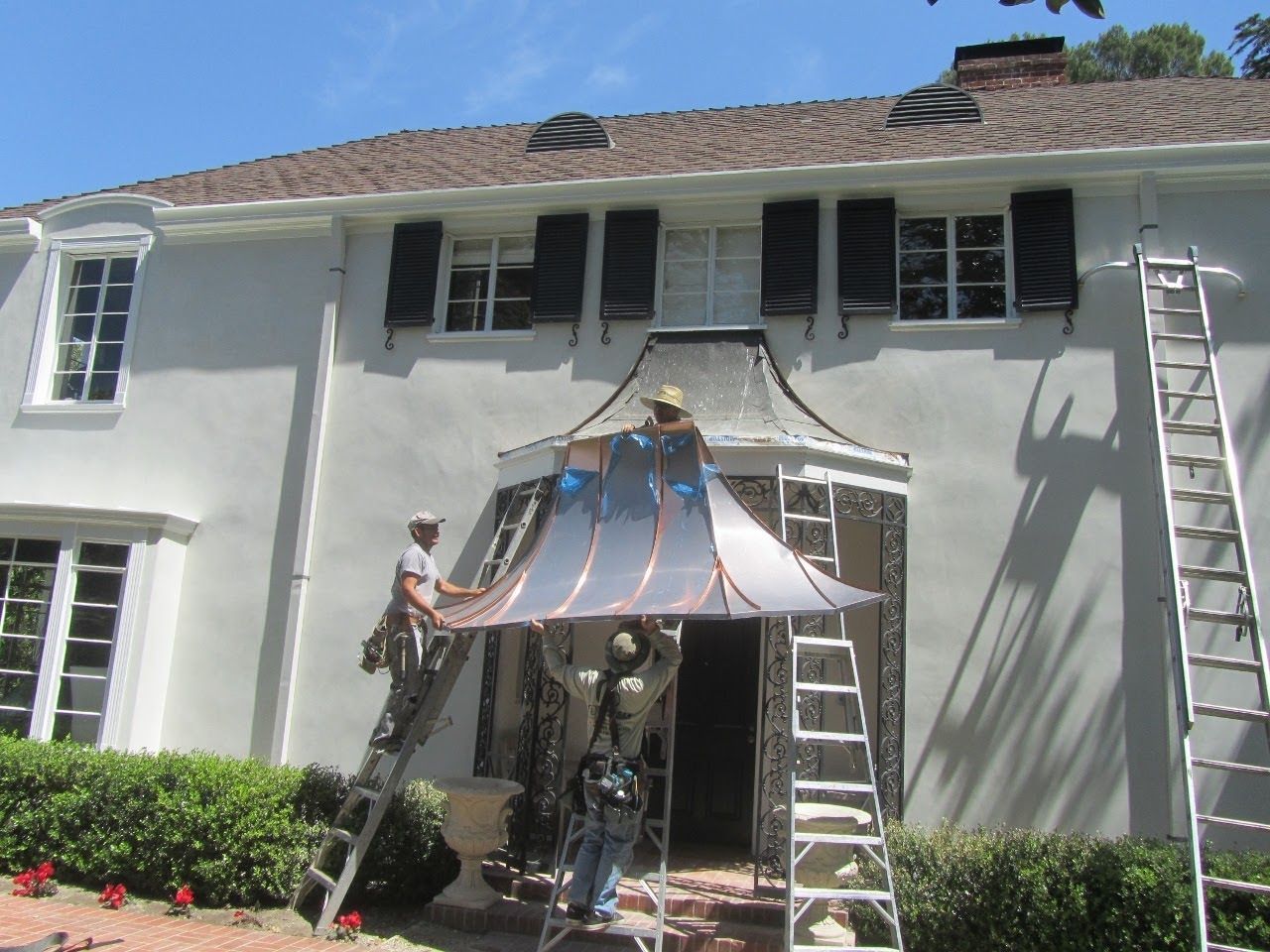 Men install a copper awning over a doorway of a two-story white house.