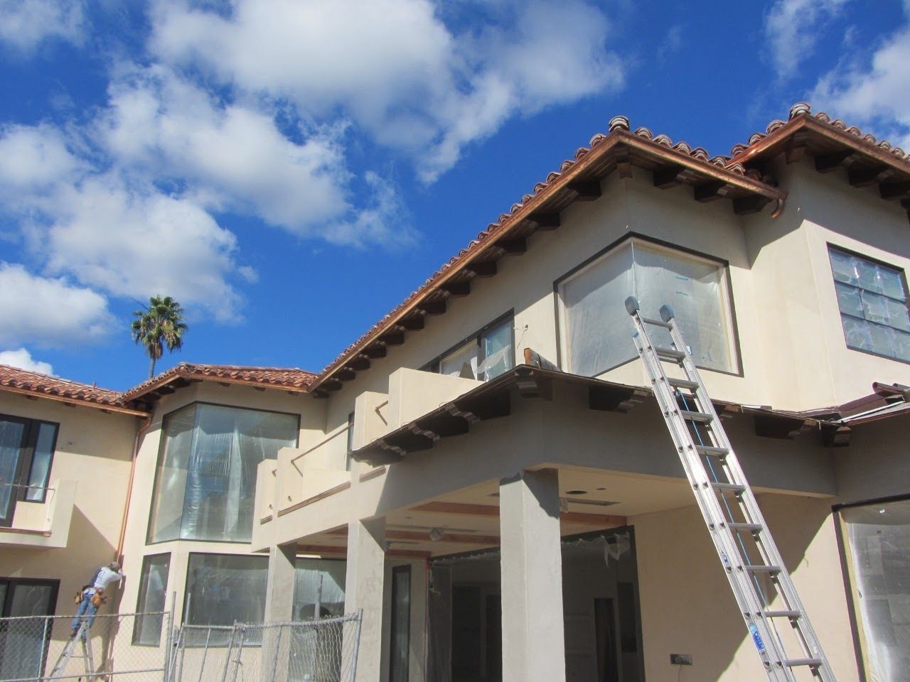 A two-story house under construction with a ladder against the building; blue sky with clouds.