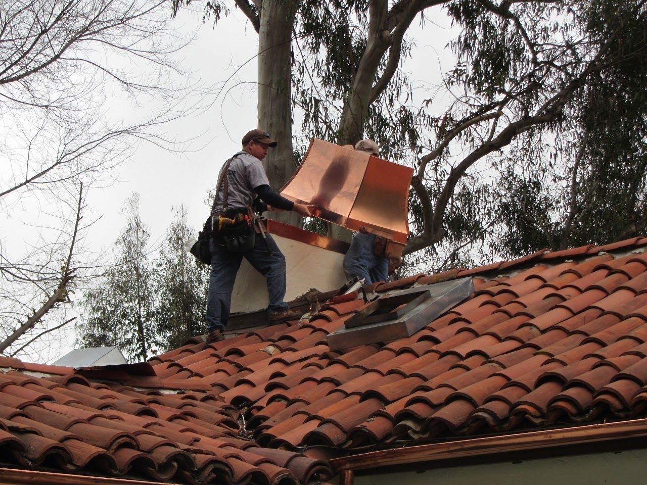 Two roofers installing copper flashing on a tiled roof. Overcast day.