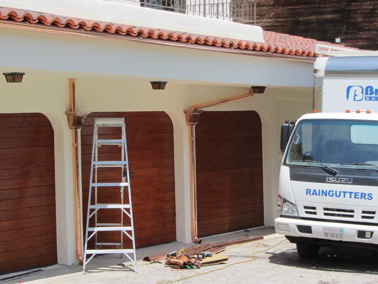 Garage with copper gutters being installed by a company truck; ladder in front of doors.