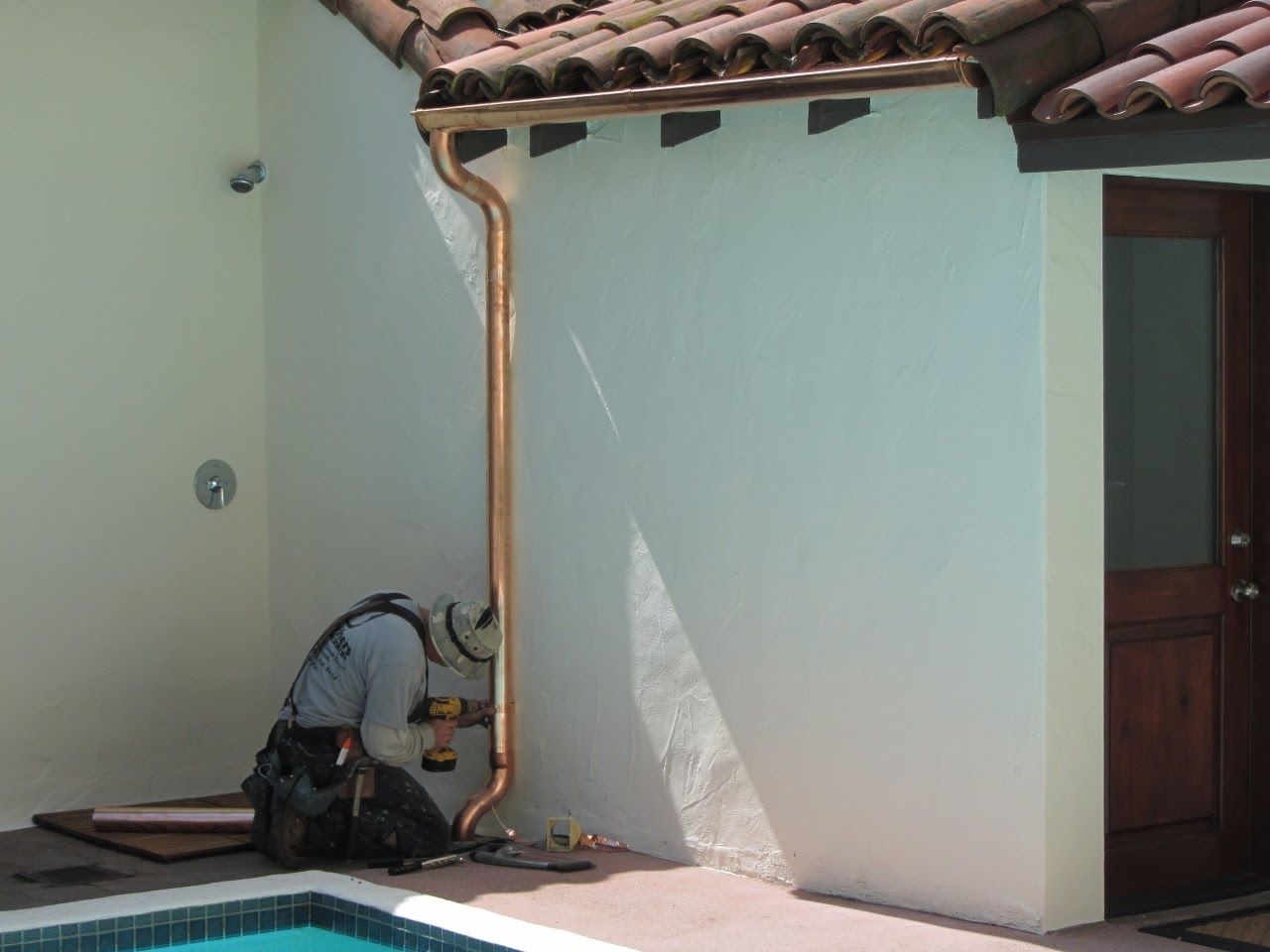 Man installing copper rain gutter next to a white stucco wall and a pool.