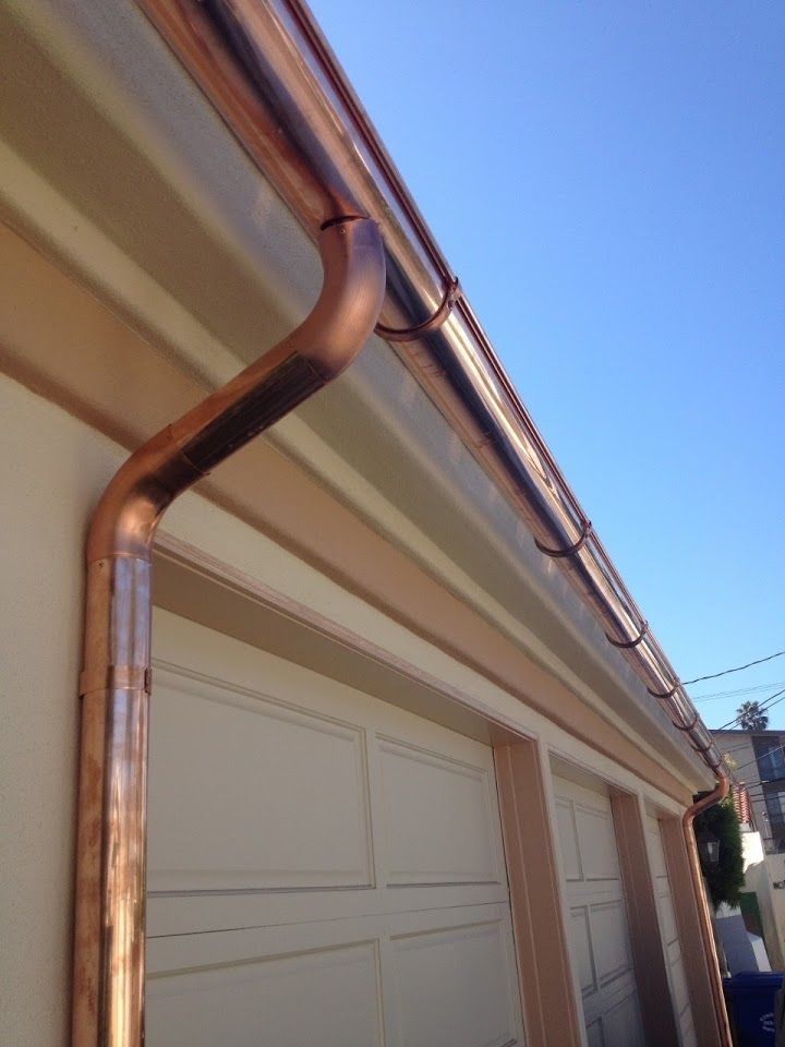 Copper gutters on a light-colored building, with a downspout near the garage door against a blue sky.
