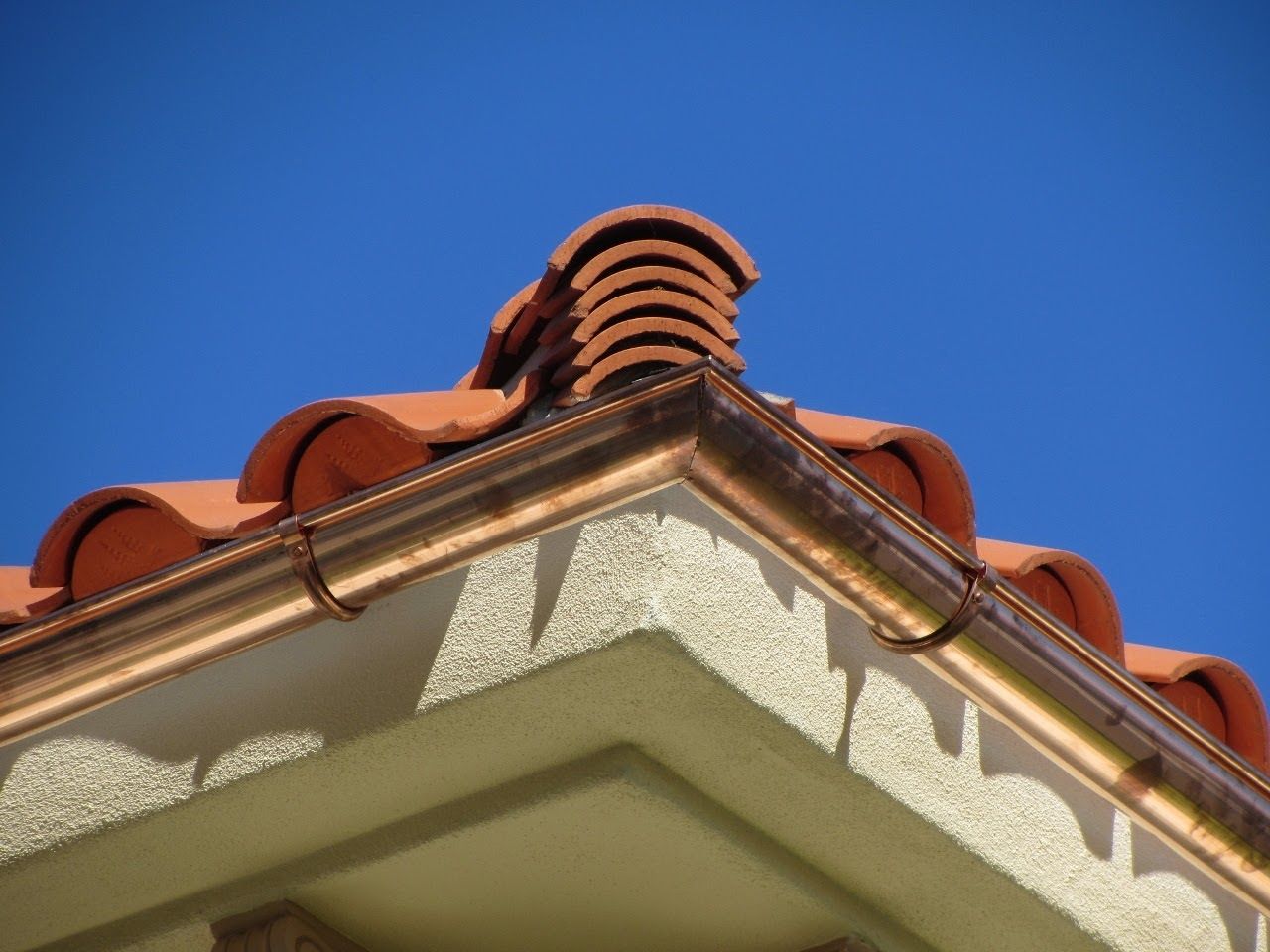 Copper gutters and red tile roof on a stucco building against a clear blue sky.