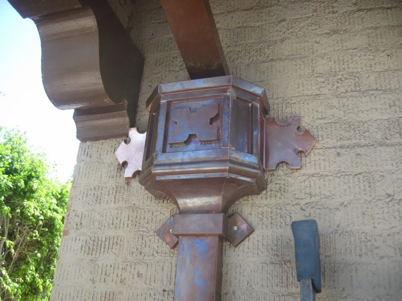 Copper downspout and gutter system on a stucco building with decorative accents.
