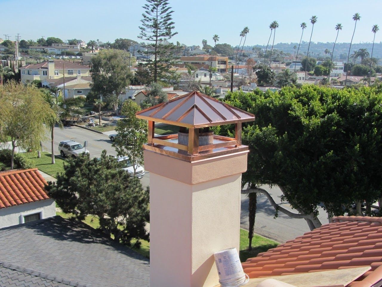 Copper chimney cap on a stucco chimney, overlooking a neighborhood on a sunny day.