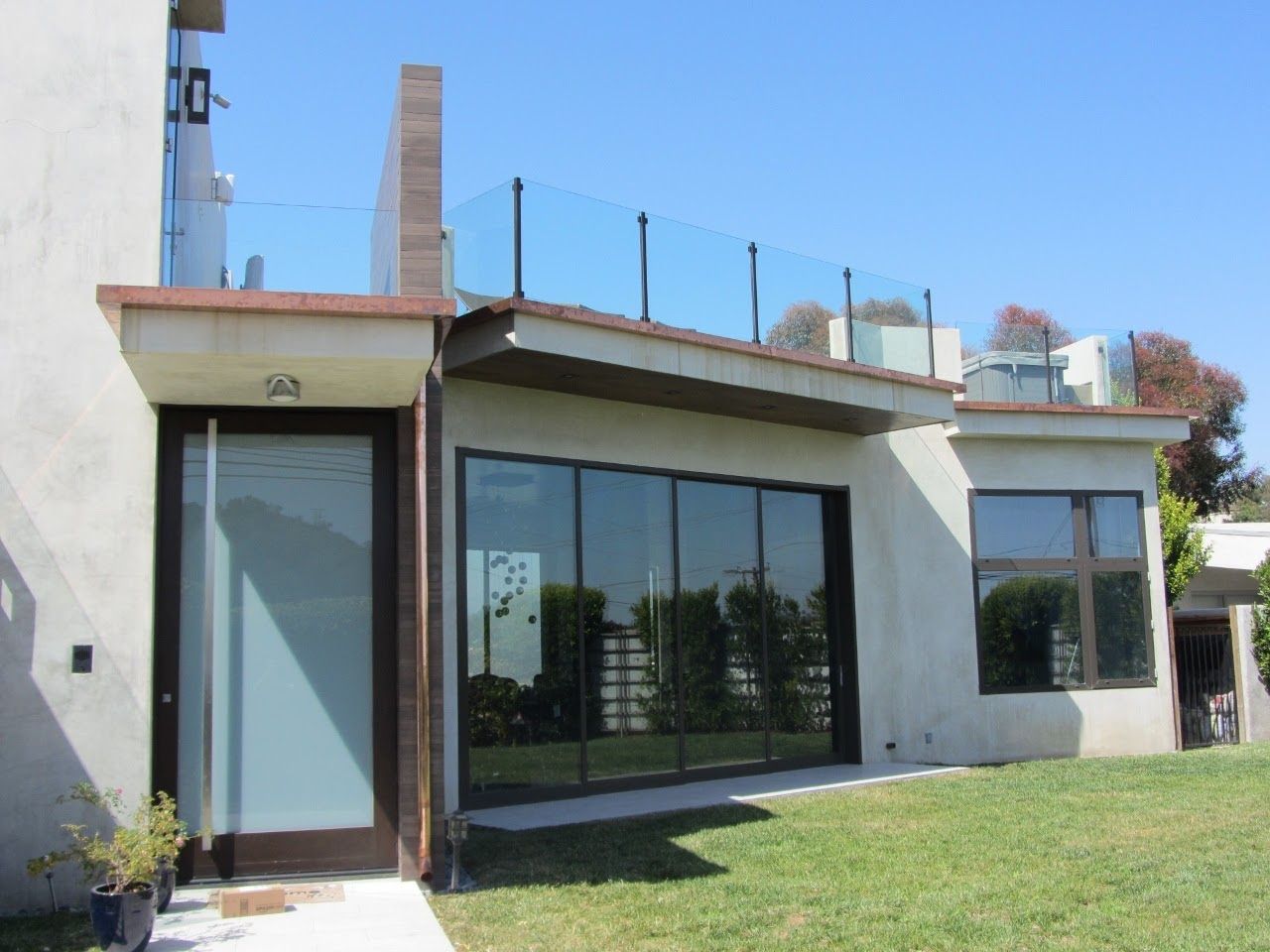 Exterior of a building with a rooftop deck, featuring glass railings and large windows.