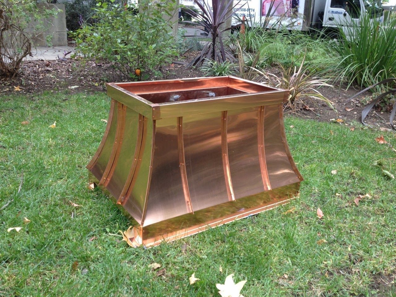 Copper planter on grass, with fluted sides and a square top.