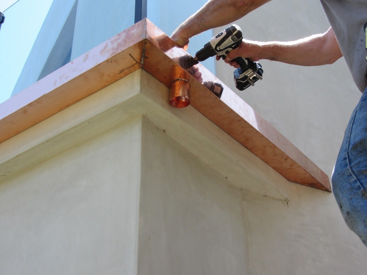 Person using a drill to install a copper gutter on a white building.