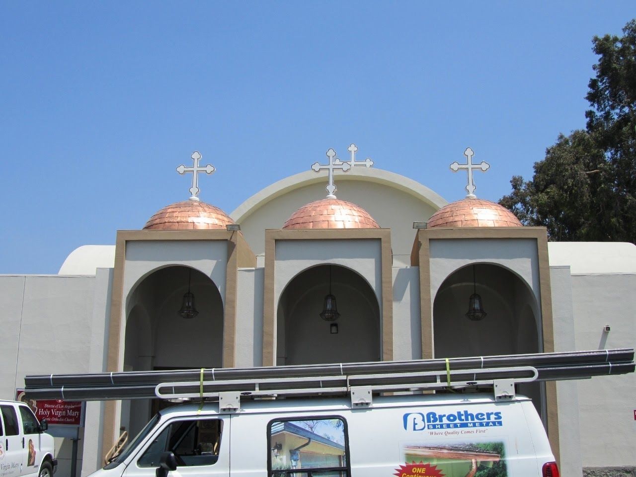 White church with copper domes, crosses, and van in front.