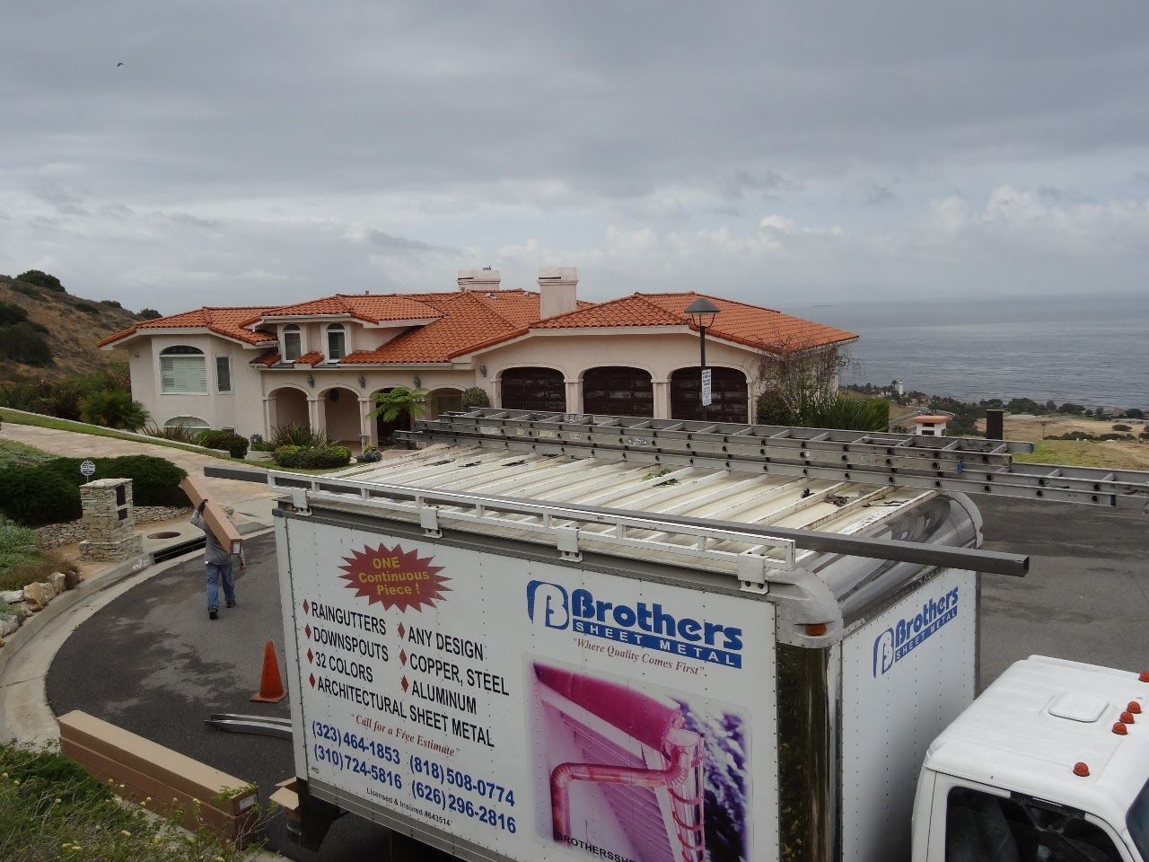 Truck in front of a house with orange tile roof overlooking the ocean. Cloudy sky.