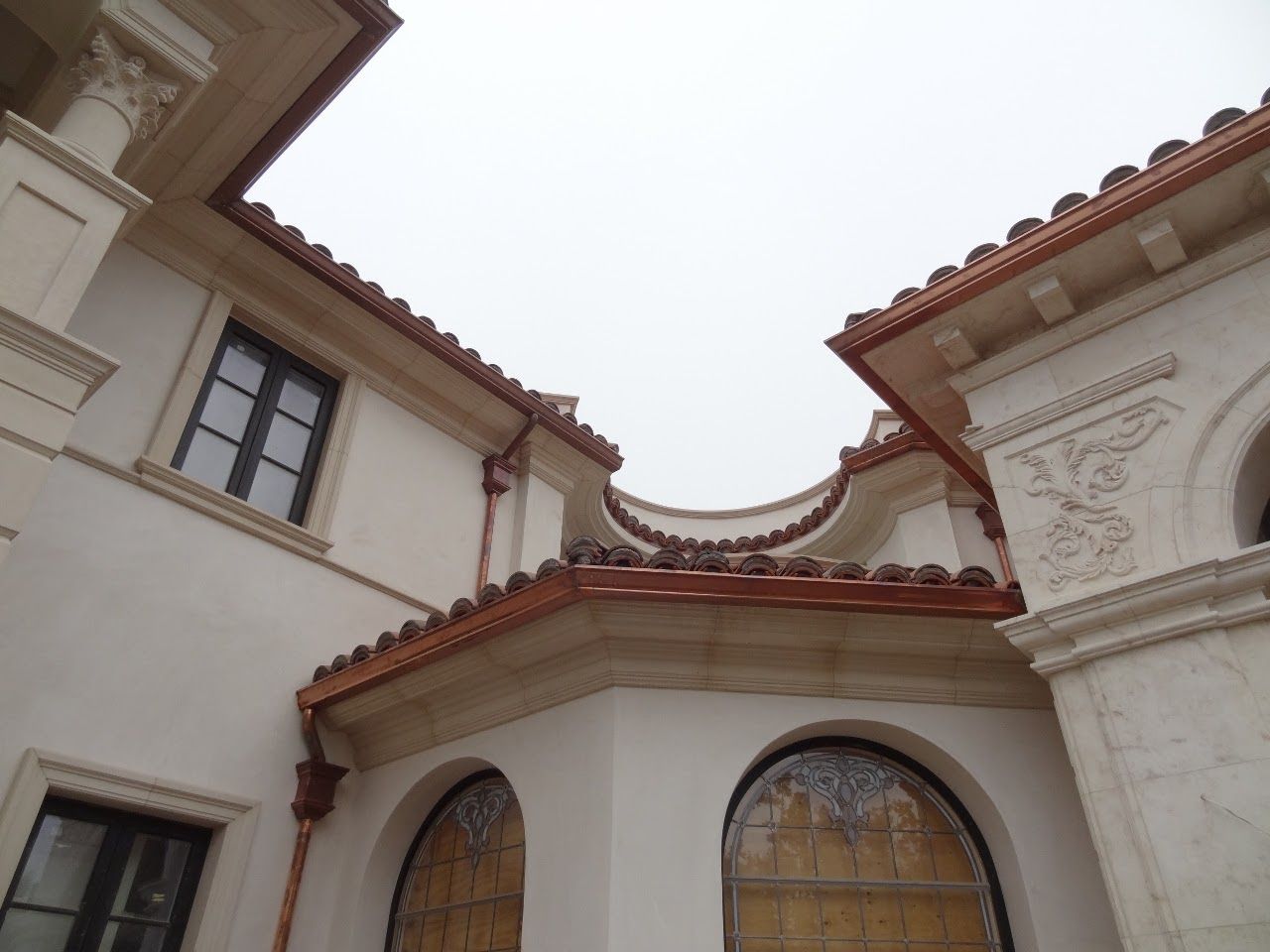 Beige building with terracotta roof tiles and copper gutters against a cloudy sky.