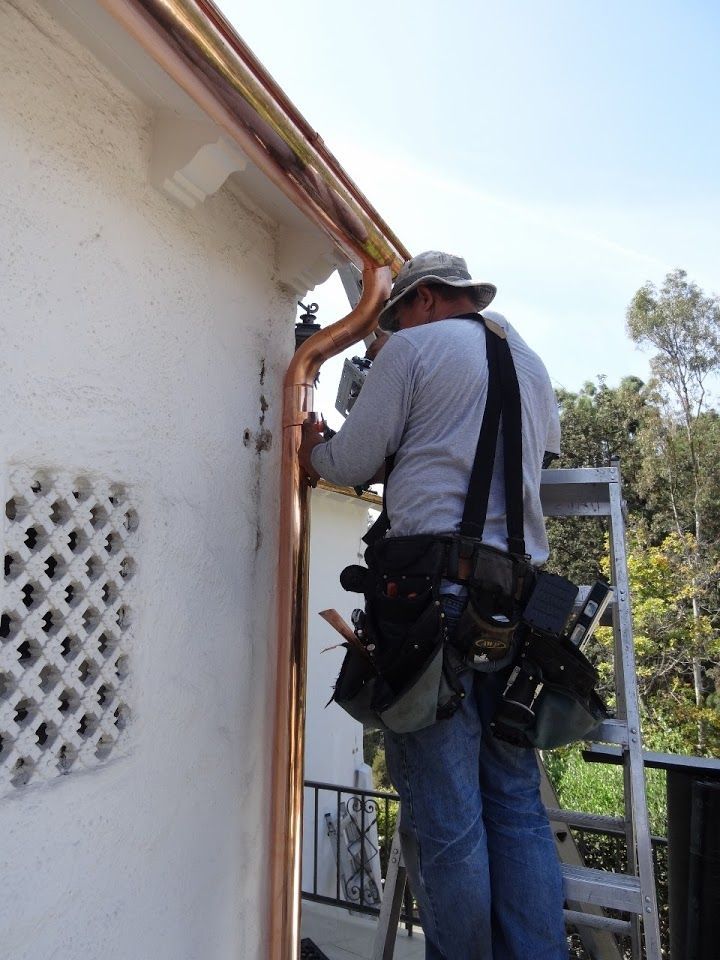 Man on ladder installing copper rain gutter on a white stucco house.