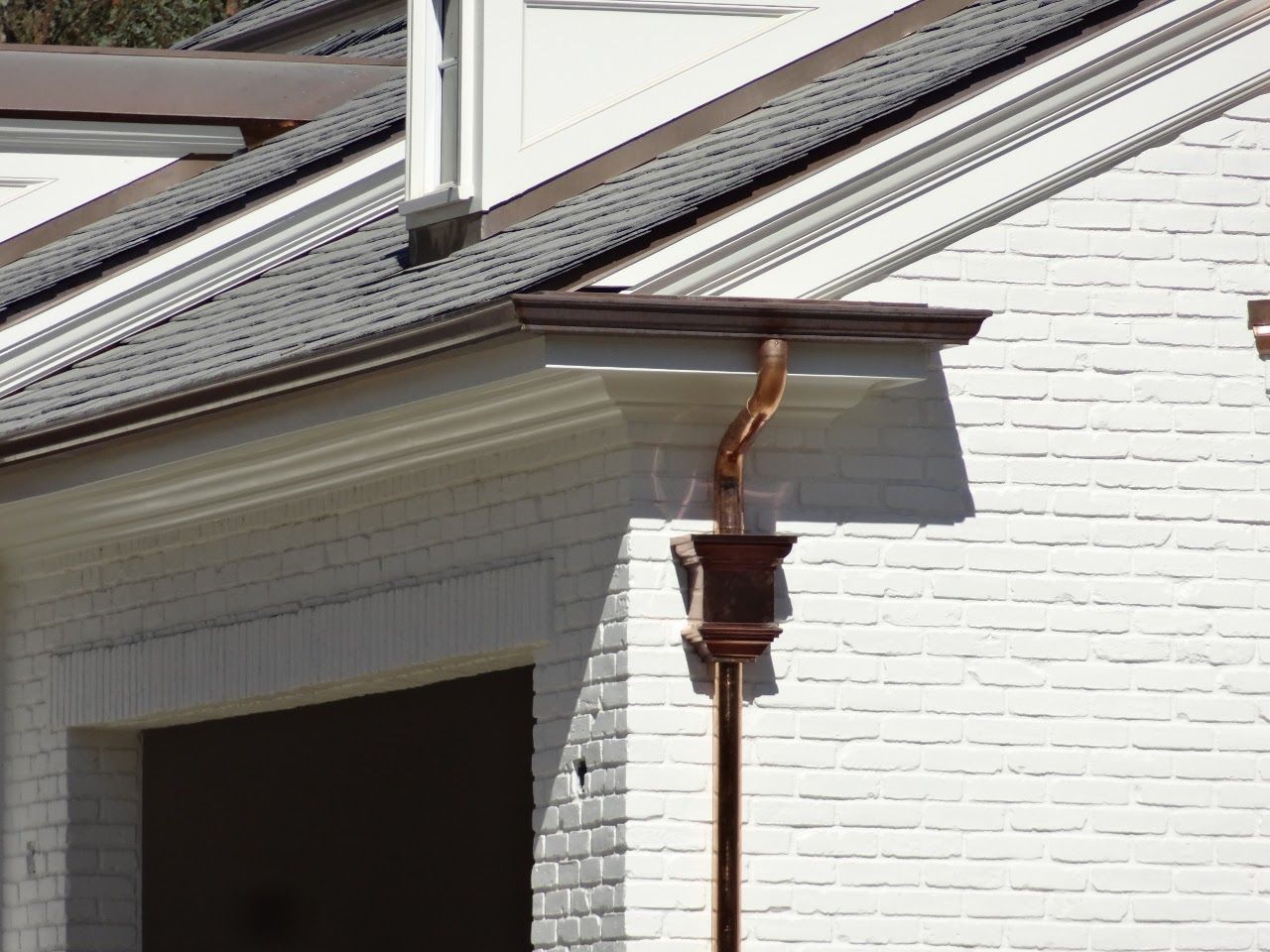 Brown gutter and downspout on a white brick building with gray roof.
