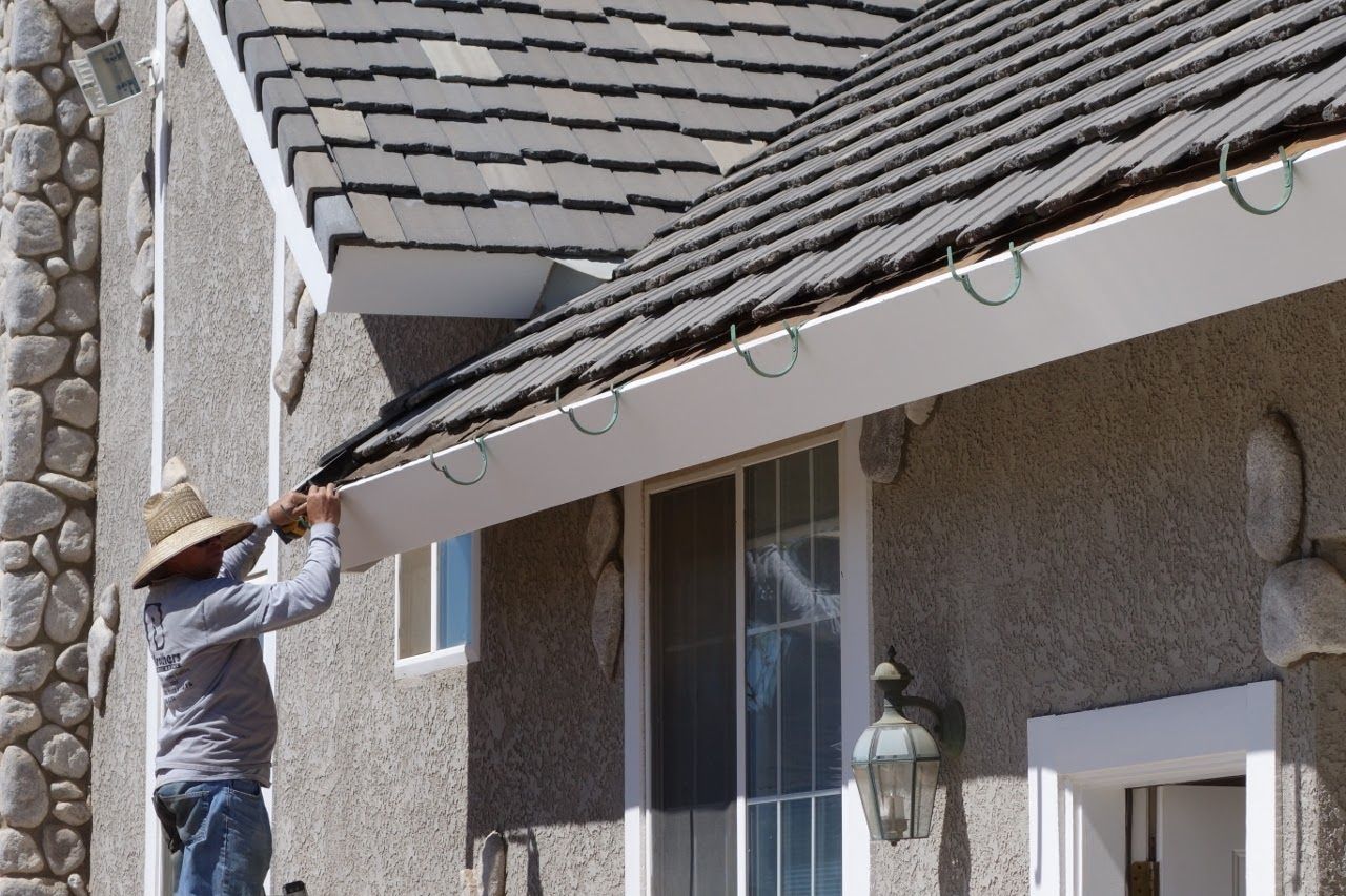 Man on ladder attaching Christmas lights to a house's gutter.