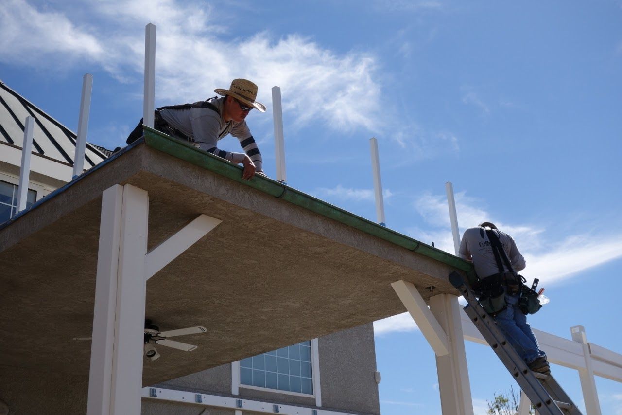 Two workers installing a railing on a porch with a blue sky background.