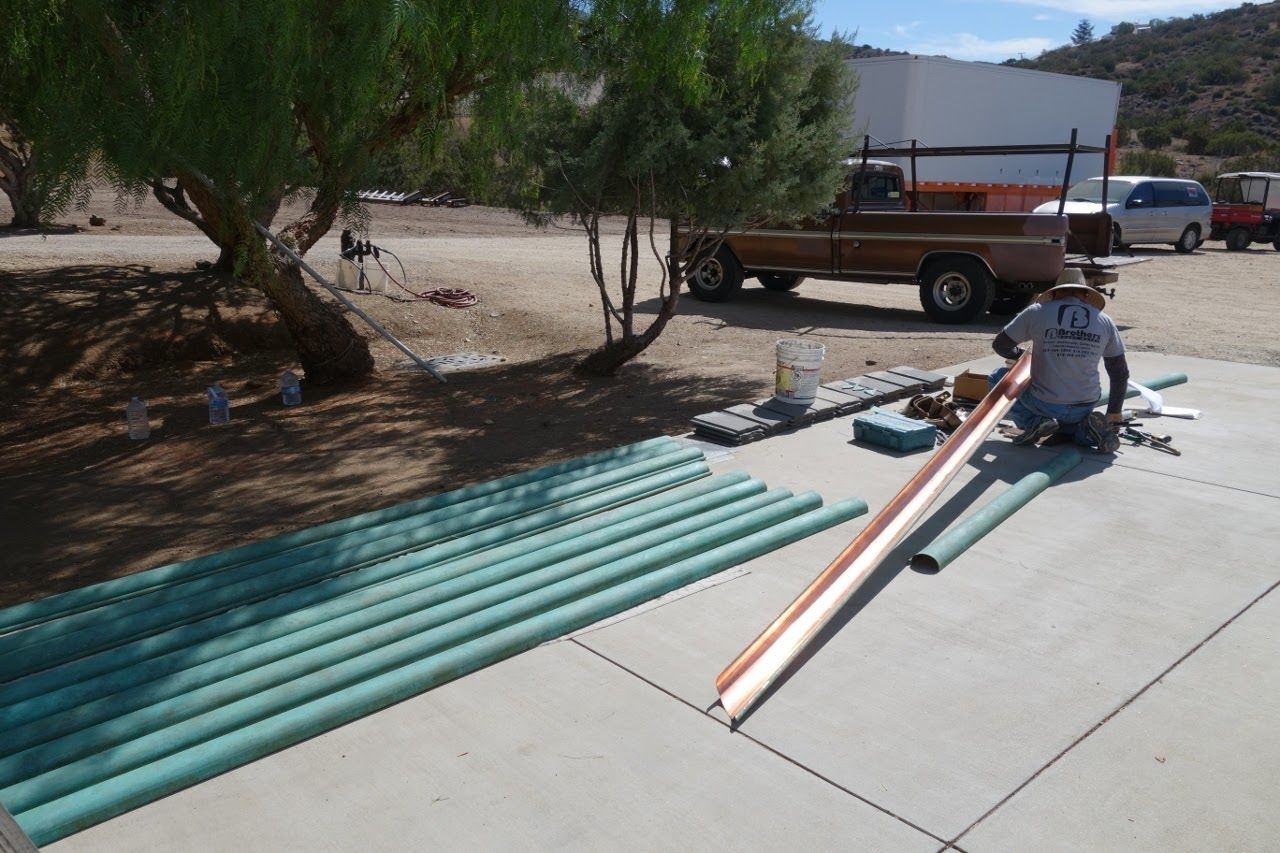 Man working with pipes outside on a sunny day, next to a truck. Green pipes lie nearby.
