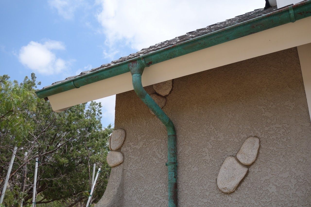 Green gutter and downspout on a stucco building with stone accents, against a blue sky.