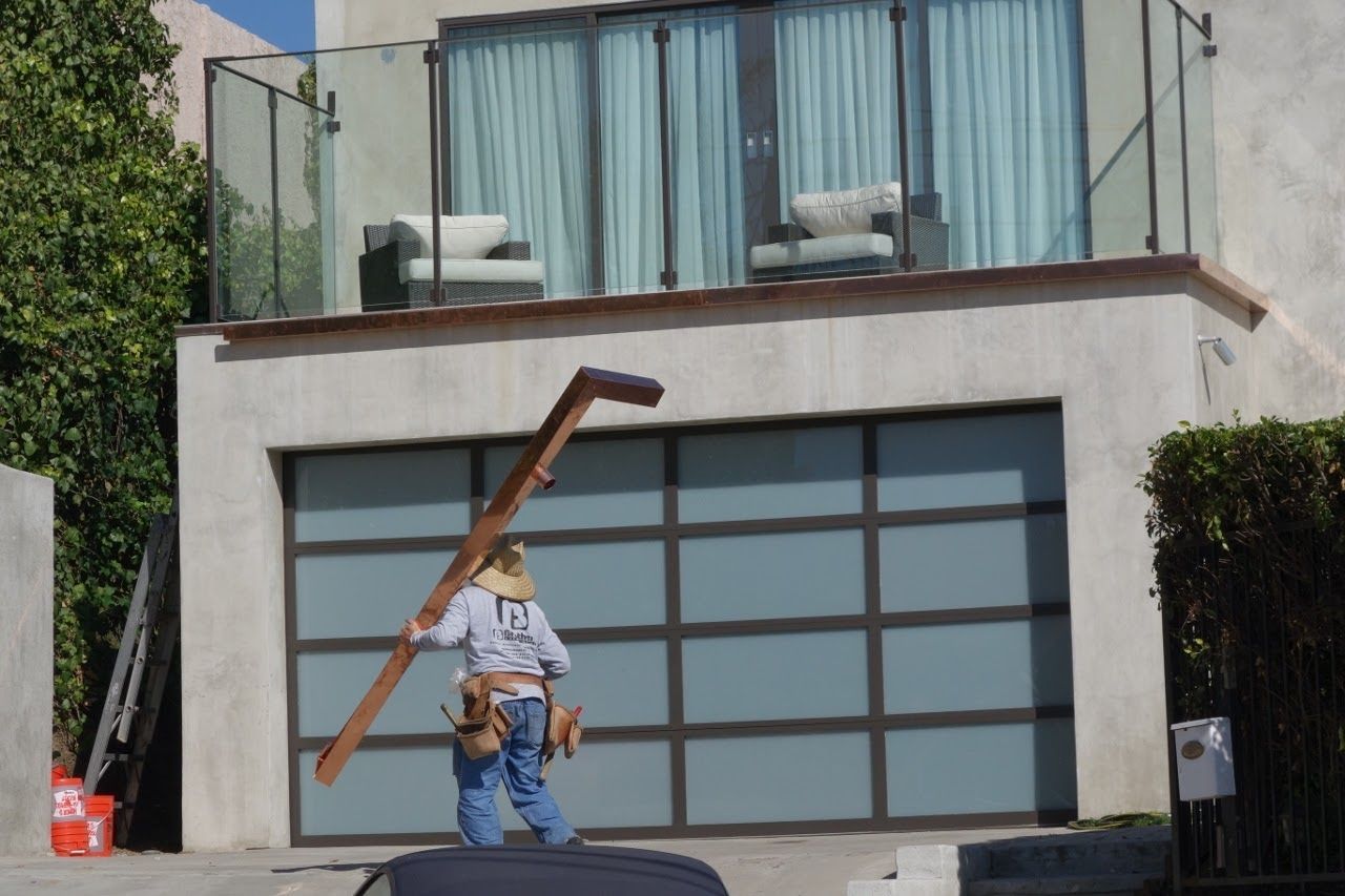 Construction worker carrying long wooden beam near a garage door. Sunny day.