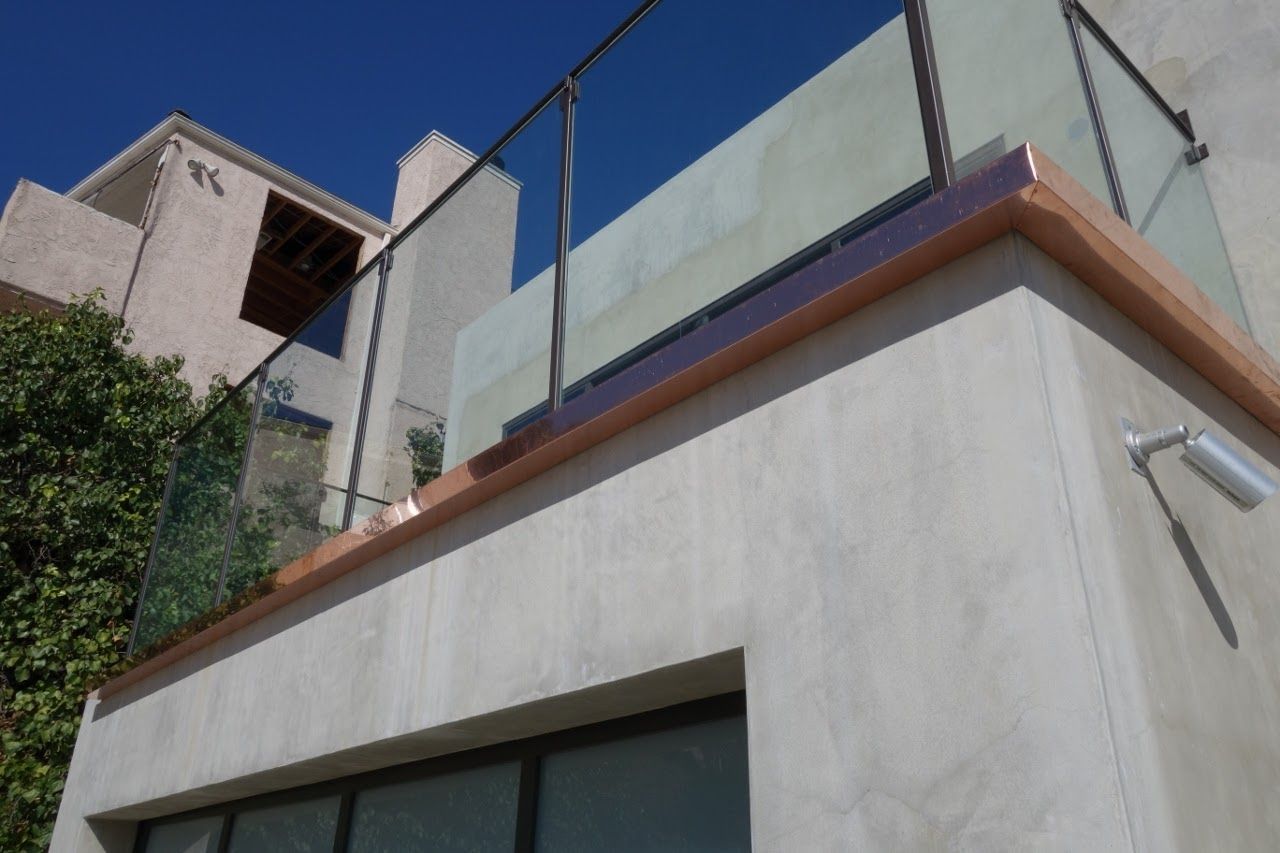 Modern building with glass and metal balcony overlooking a sunny sky.