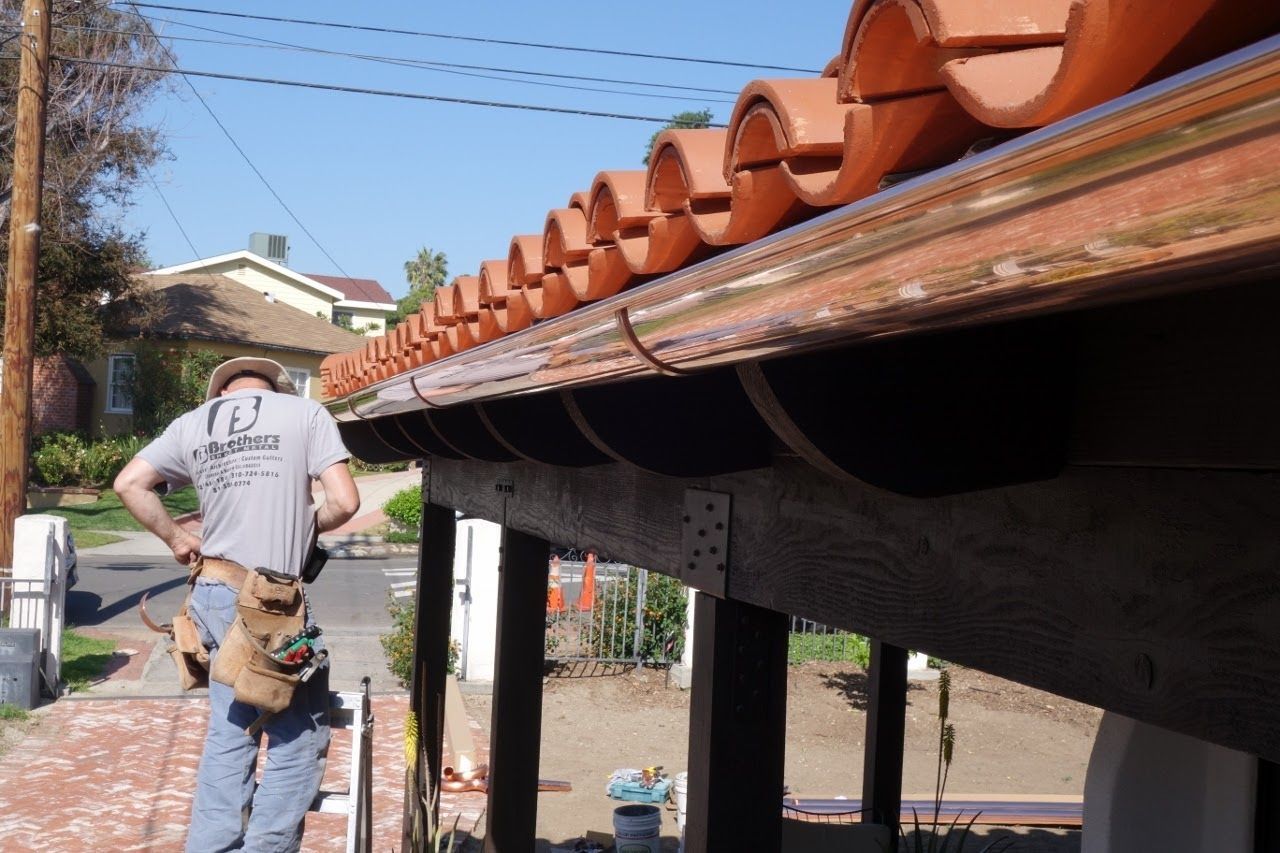 Man with tool belt inspecting terracotta tile roof and gutter.