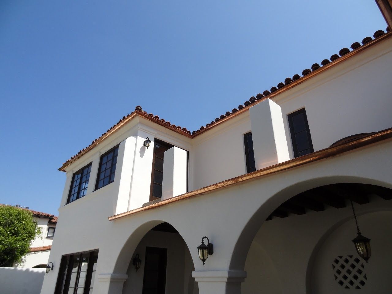 White stucco building with arched entrance and terracotta roof tiles against a blue sky.