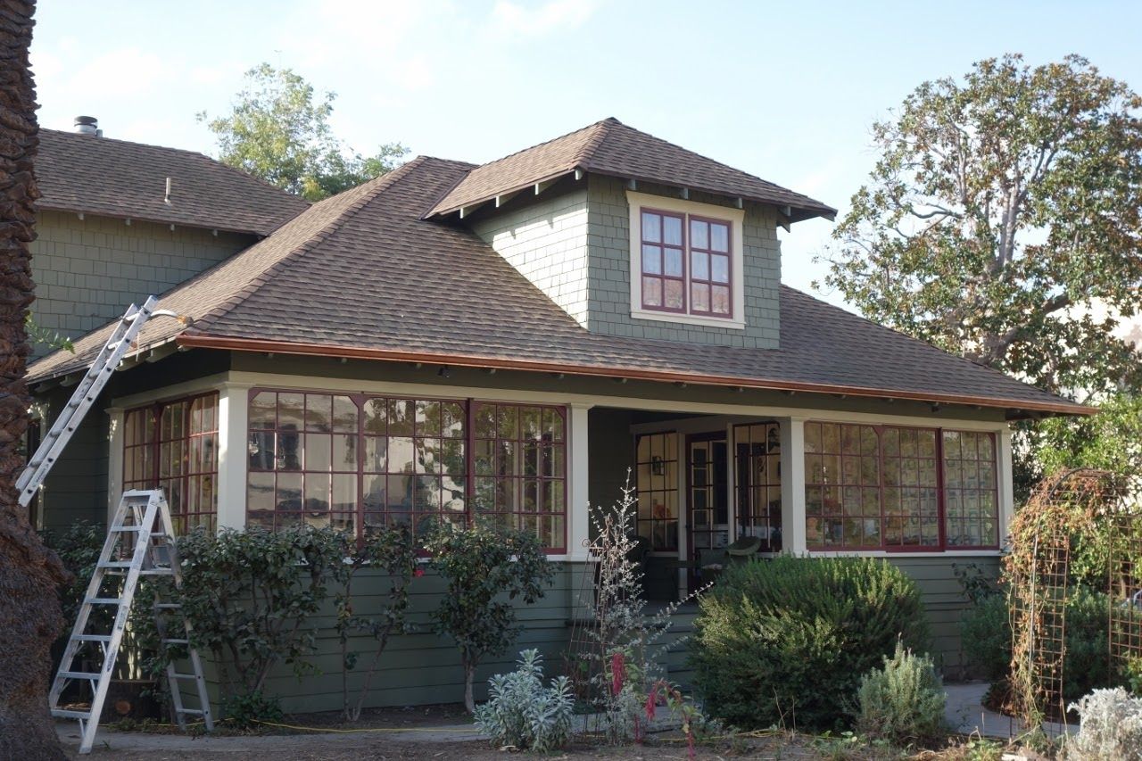 Green house with porch and dormer, ladder leaning against it.