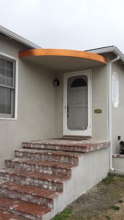 Front entrance with steps, brick facade, and beige walls. Orange-brown awning over the door.