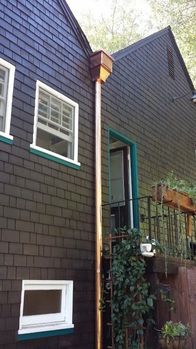 Copper gutter on a brown shingled house, next to a window and a green door.