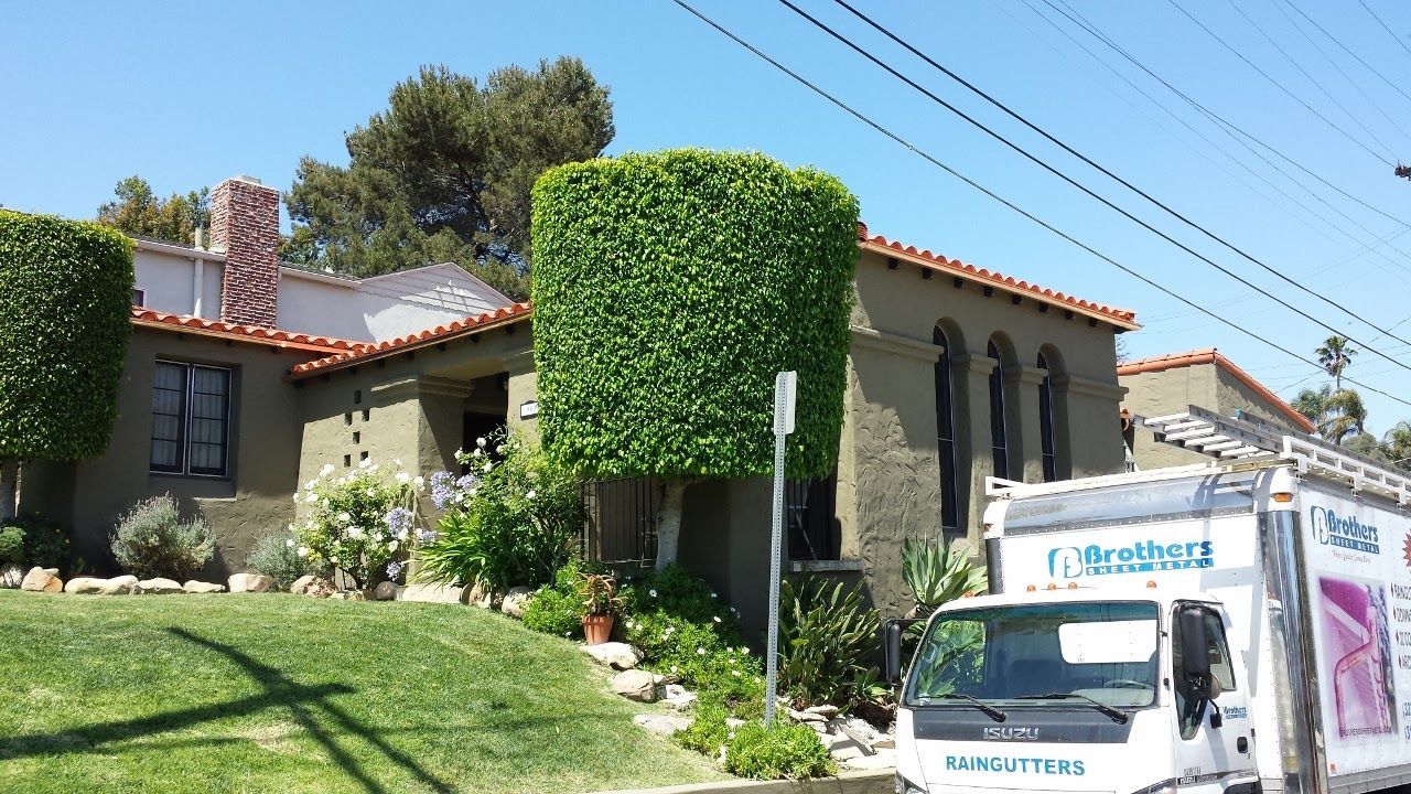 A house with manicured hedges, a white delivery truck, and overhead power lines under a sunny blue sky.