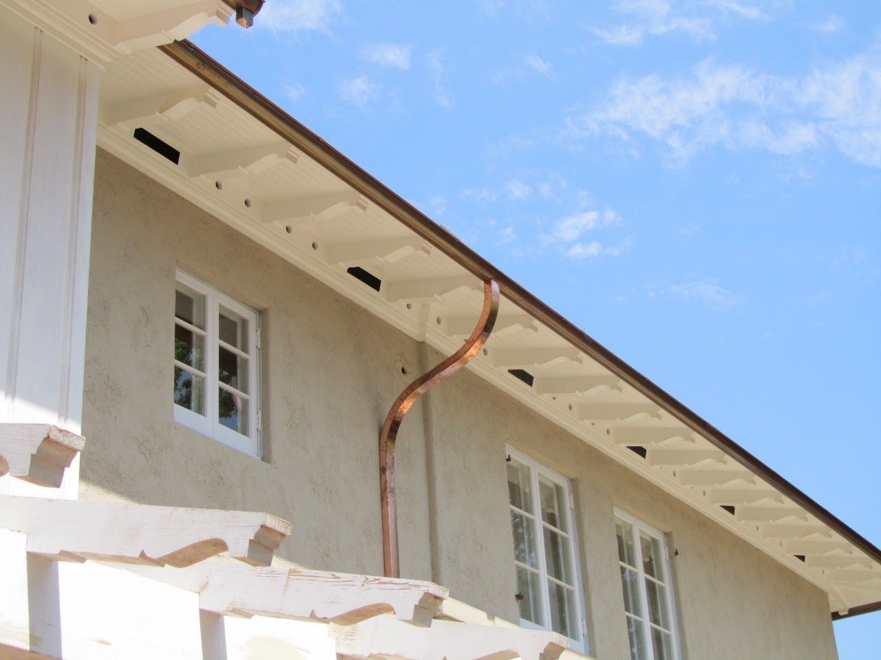 Beige building with copper downspout and white-framed windows against a blue sky.