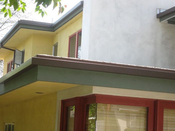 Two-story house with yellow and white walls, brown roof and trim, red window frames, and a green awning.