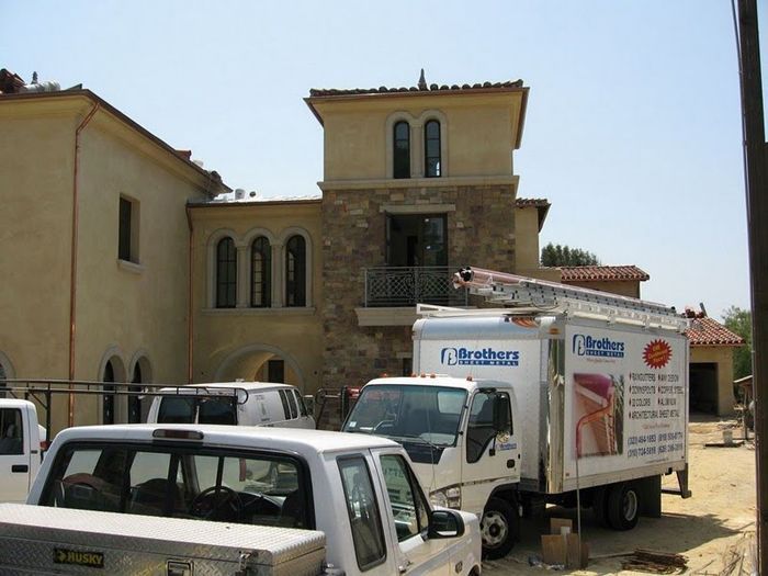 Construction site: Trucks and vehicles in front of a two-story stucco building with stone accents.