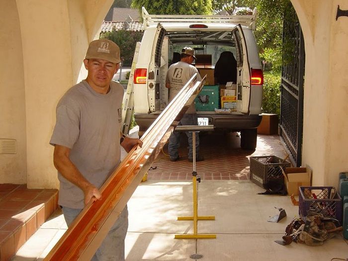 Man holding wood trim in front of a van, working near a house entrance.