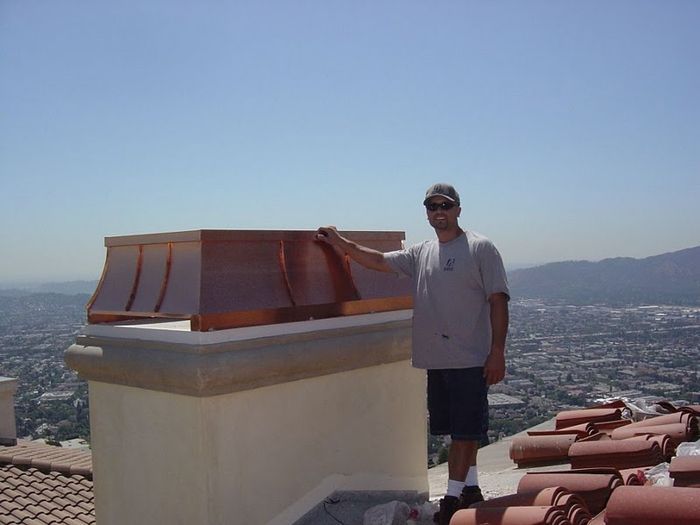 Man beside a copper chimney cap on a rooftop, cityscape in the background.