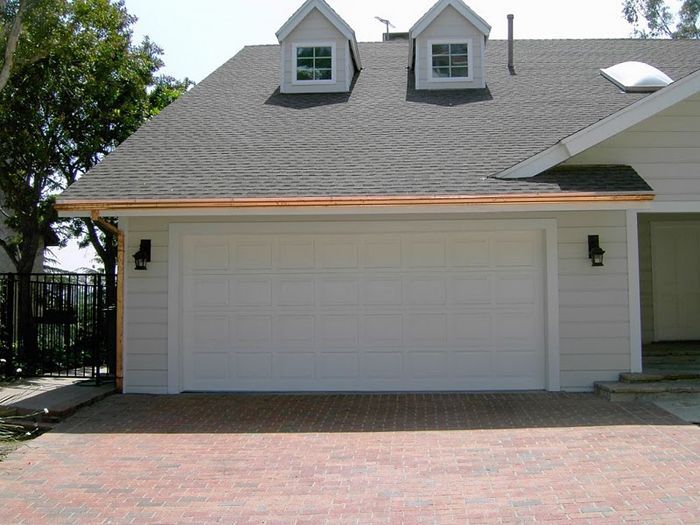 White garage door with copper gutters, brick driveway, and small dormer windows.