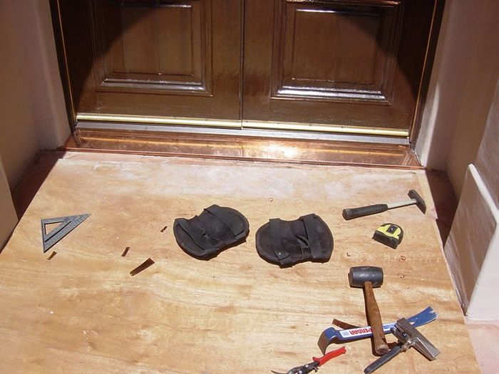 Door threshold under construction, with tools and rubber pads on a wooden surface.