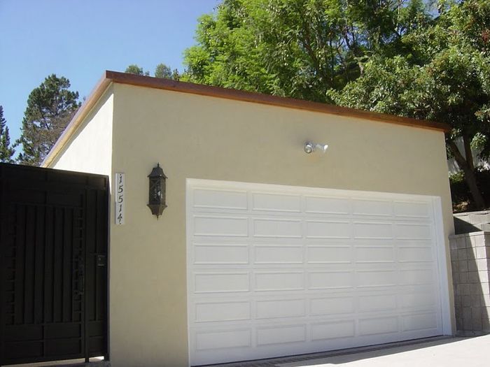 Beige garage with a white door, address 35524, next to a black gate, and green trees in the background.